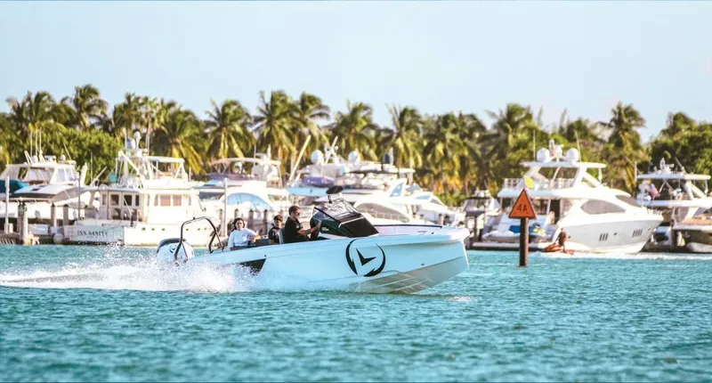 Slide: The Image of 2021 Axopar Spyder 22 cruising in a vibrant marina with palm trees and yachts. - 2