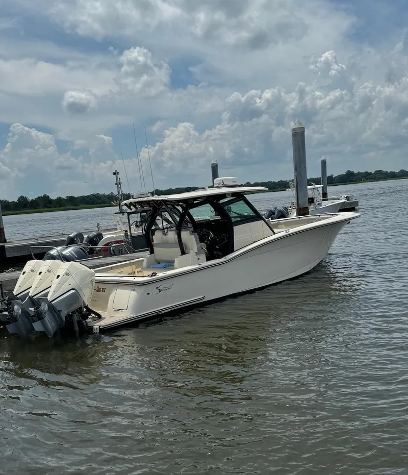 The Image of 2023 Scout 355 LXF boat docked on a calm lake under a cloudy sky. - 0