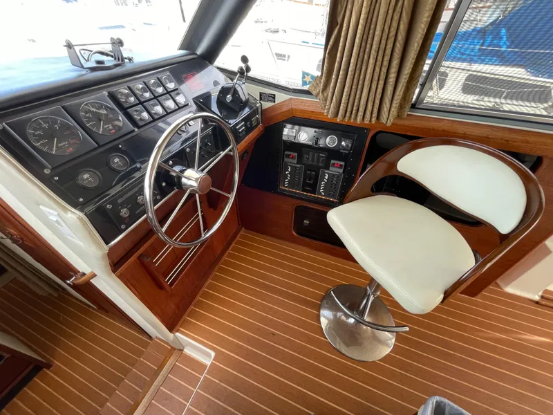 Slide: The Image of 1989 Bayliner 3288 helm with steering wheel, control panel, and swivel chair on wooden flooring. - 14