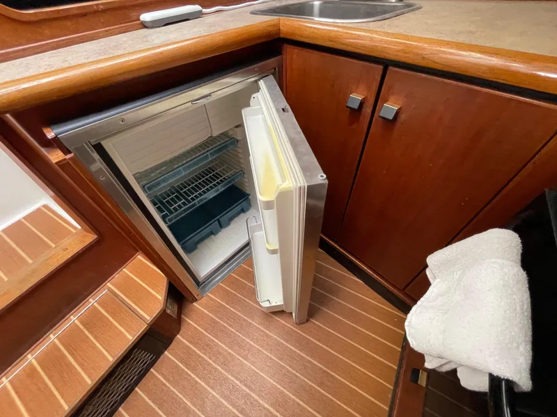 Slide: The Image of 1989 Bayliner 3288 yacht interior with open fridge and wooden cabinetry. - 19