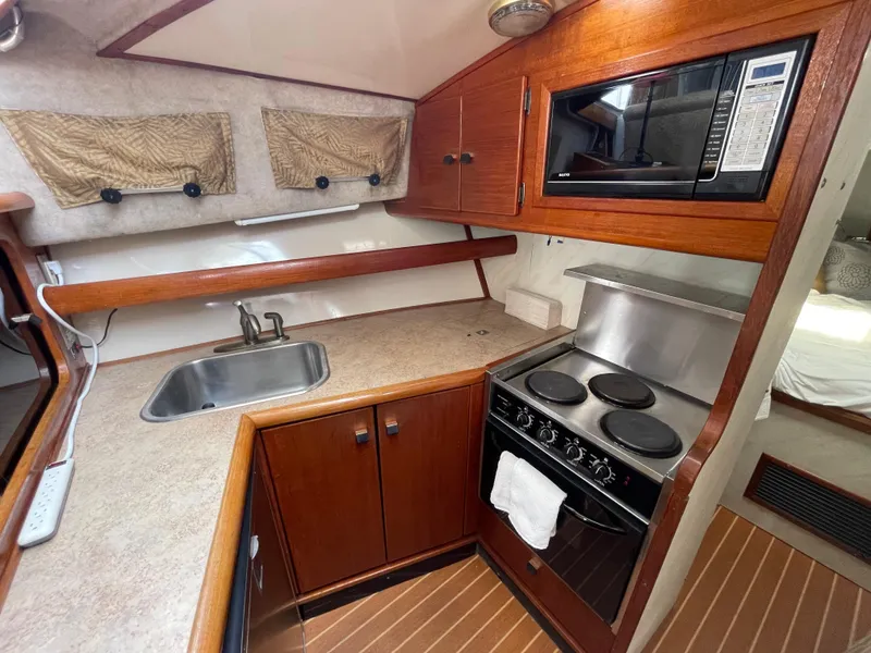Slide: The Image of 1989 Bayliner 3288 galley with stove, sink, microwave, and wooden cabinetry. - 20