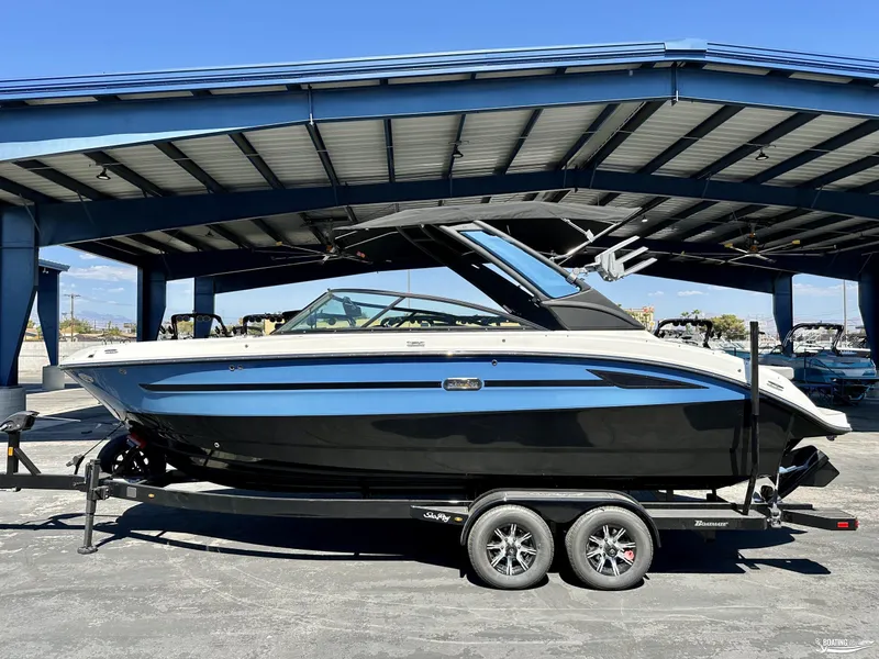 Slide: The Image of 2025 Sea Ray SDX 250 Surf boat on trailer under a metal canopy. - 0