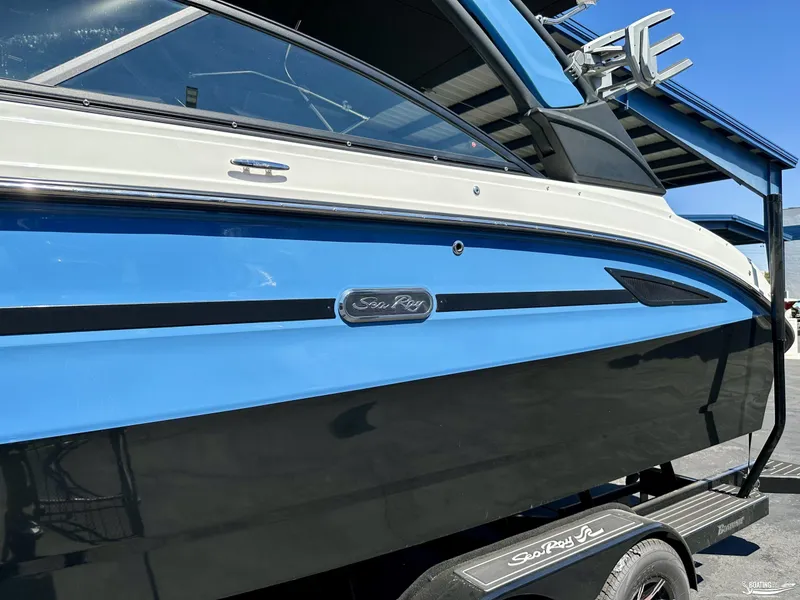 Slide: The Image of 2025 Sea Ray SDX 250 Surf boat, blue and black exterior, on a trailer. - 1