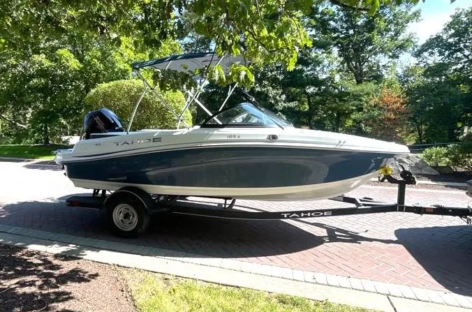 Slide: The Image of 2024 Tahoe 185 S boat on trailer, parked in a leafy driveway. - 0
