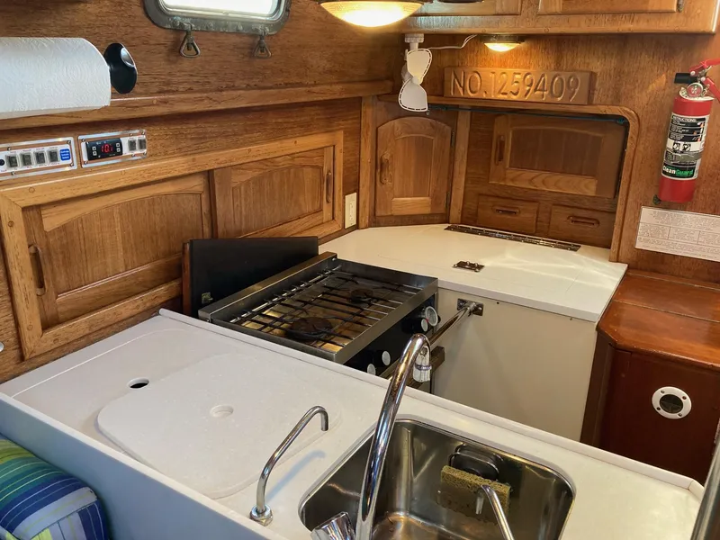 Slide: The Image of Interior of 1992 Pacific Seacraft 37 Cutter, featuring a compact kitchen with stove and sink. - 11