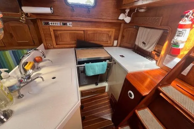 Slide: The Image of Interior of 1992 Pacific Seacraft 37 Cutter, featuring a compact kitchen with wooden cabinetry. - 21