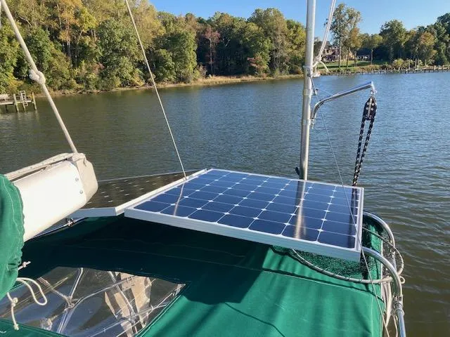 Slide: The Image of 1992 Pacific Seacraft 37 Cutter with solar panel on deck, moored by a forested shoreline. - 40
