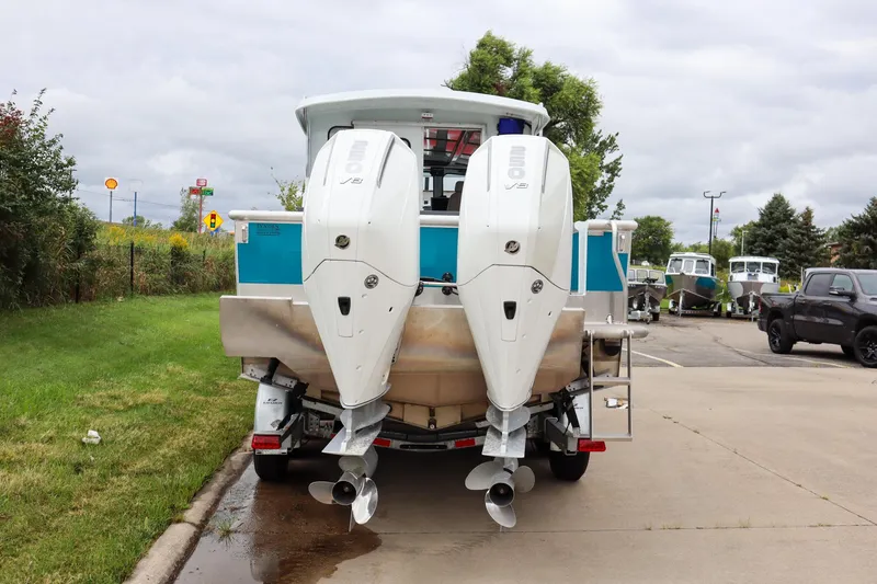 Slide: The Image of 2024 Hewescraft 270 Pacific Explorer with dual outboard motors, parked on a concrete driveway. - 3