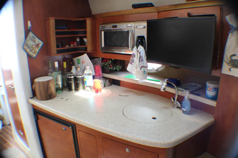 Slide: The Image of 2007 Rinker 350 Express Cruiser kitchen with countertop, sink, microwave, and storage shelves. - 9
