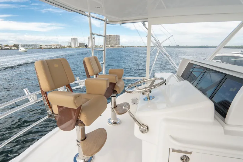 Slide: The Image of Hatteras GT60 2010 yacht helm with beige seats, overlooking calm waters and cityscape. - 13
