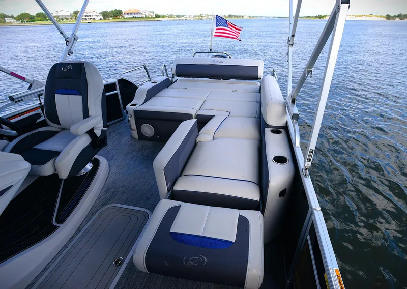 Slide: The Image of 2022 Barletta Corsa 25U pontoon boat interior with plush seating and American flag on a lake. - 18