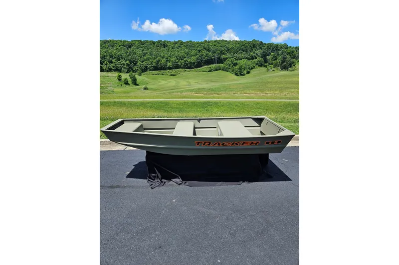 Slide: The Image of 2025 Tracker Grizzly 1036 Utility boat on pavement, green landscape background. - 26