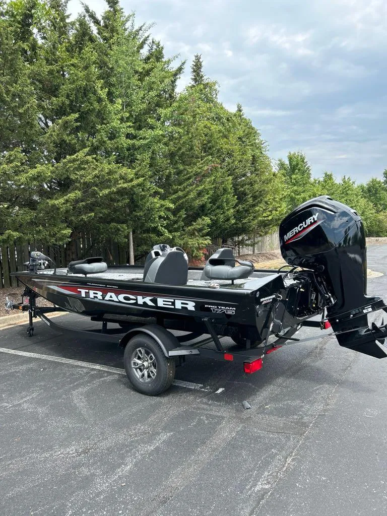 Slide: The Image of 2025 Tracker Pro Team 175 boat with Mercury engine, parked outdoors near trees. - 3
