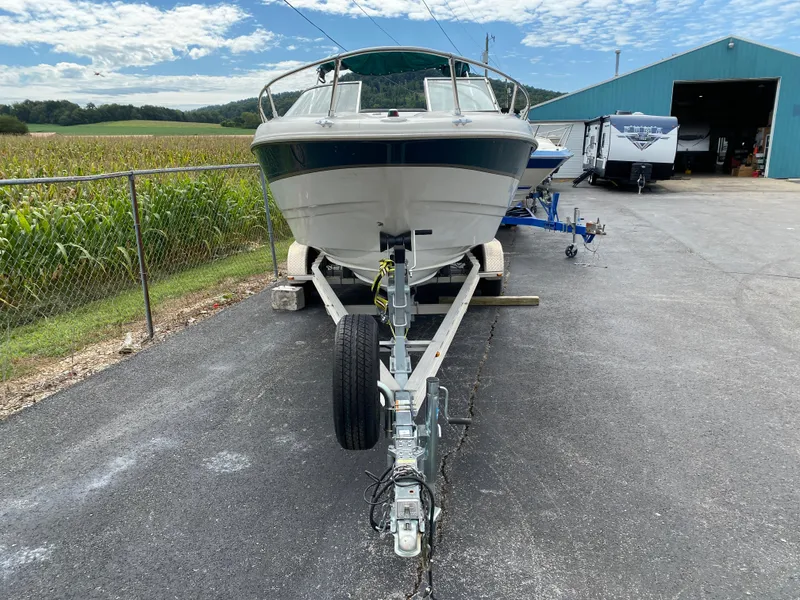 Slide: The Image of 2000 Bayliner 2352 Capri DX/LX boat on trailer, parked near a field and blue building. - 33