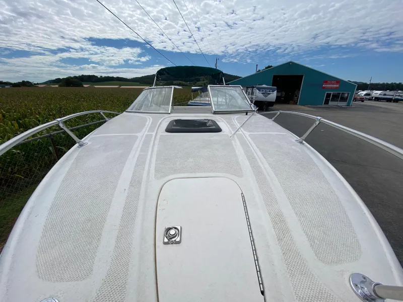 Slide: The Image of 2000 Bayliner 2352 Capri DX/LX boat deck with open hatch, parked near a blue building. - 9