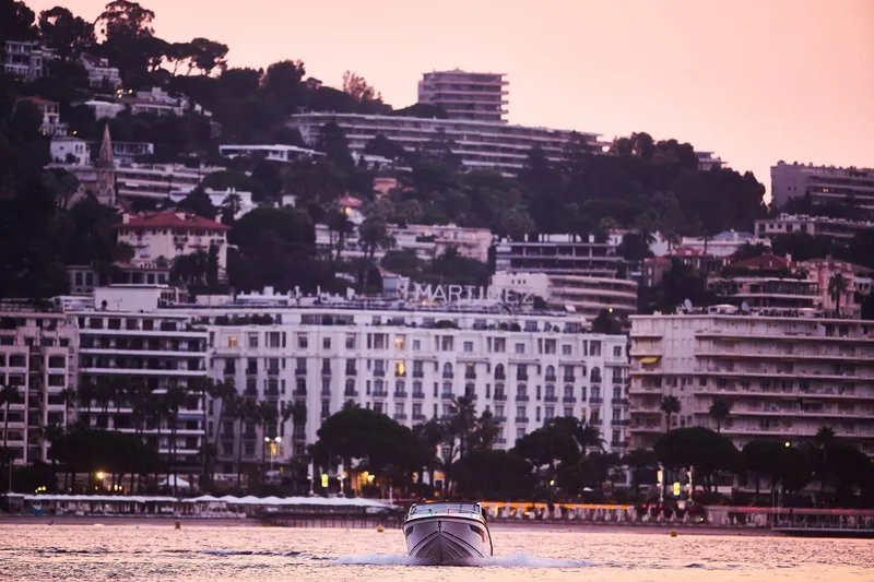 Slide: The Image of 2024 Skamander Sorrento boat cruising near coastal cityscape at sunset. - 2