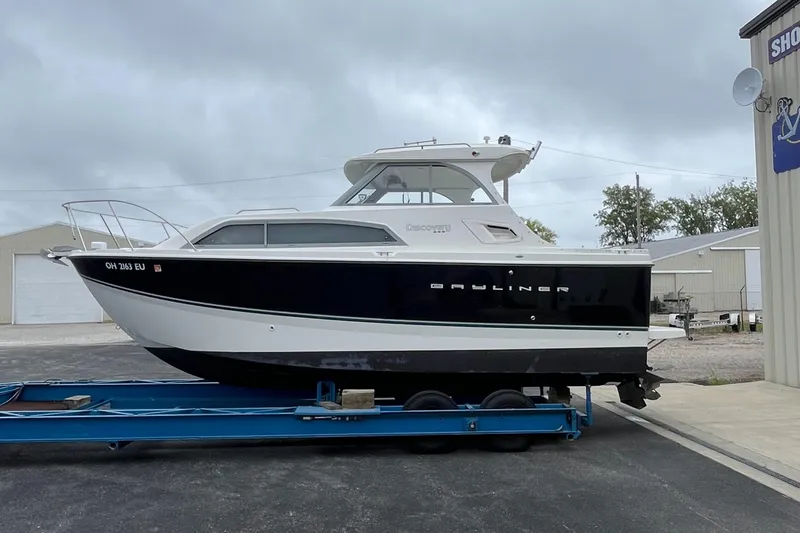 Slide: The Image of 2011 Bayliner 266 Discovery boat on trailer, parked outdoors under cloudy sky. - 3