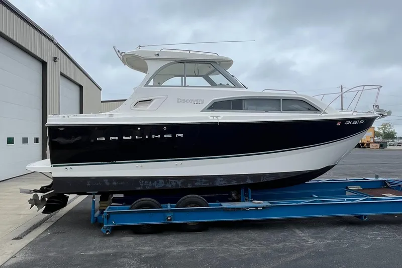Slide: The Image of 2011 Bayliner 266 Discovery boat on trailer, parked near a warehouse. - 6