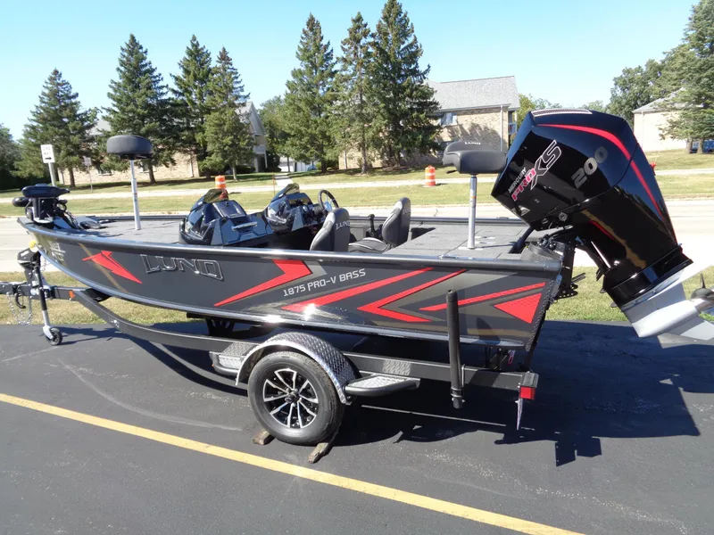 Slide: The Image of 2025 Lund 1875 Pro-V Bass XS boat on trailer, parked outdoors. - 2