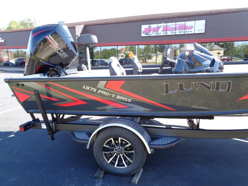 Slide: The Image of 2025 Lund 1875 Pro-V Bass XS boat on trailer, parked outside a store. - 3