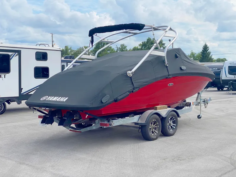 Slide: The Image of 2014 Yamaha Boats 242 Limited S covered on trailer, red hull, parked outdoors. - 7