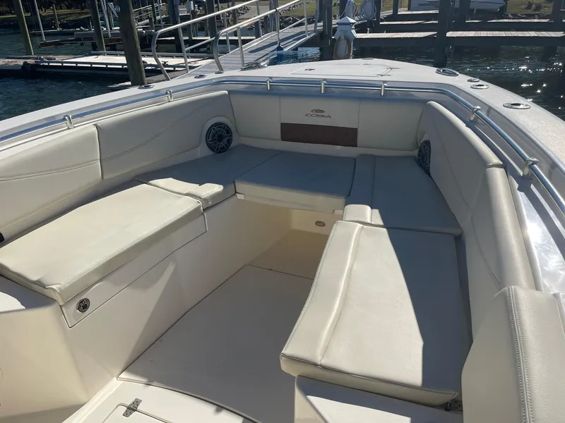 Slide: The Image of 2023 Cobia 320 CC boat interior with cushioned seating and dock view. - 23