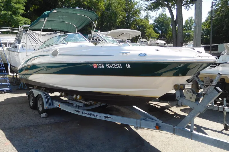 The Image of 2002 Sea Ray 240 Sundeck boat on trailer, green and white, parked outdoors. - 0