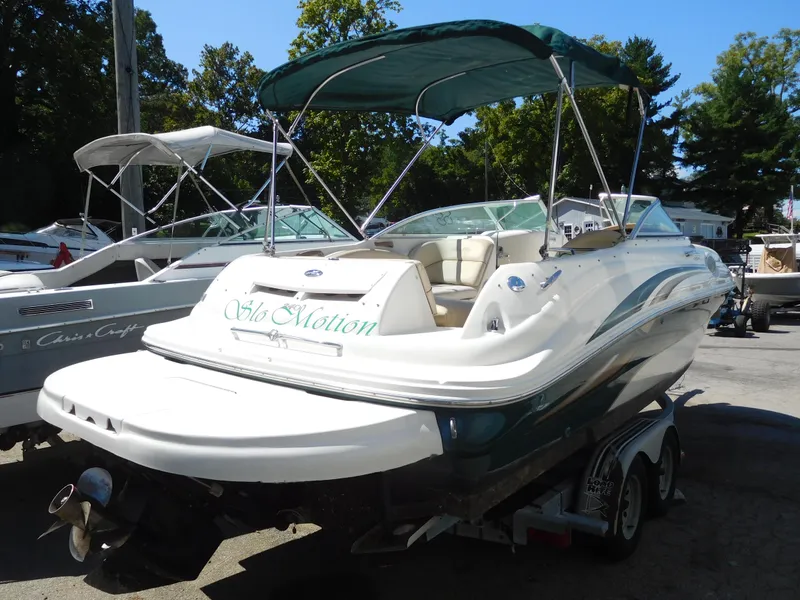 Slide: The Image of 2002 Sea Ray 240 Sundeck boat with green canopy on trailer, parked outdoors. - 2
