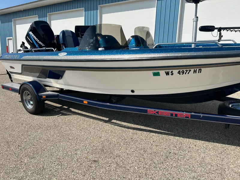 Slide: The Image of 2005 Skeeter WX 1880 boat on trailer, parked outdoors near blue building. - 27