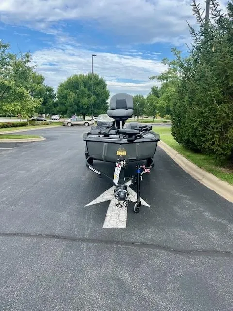 Slide: The Image of 2025 Tracker Pro 170 boat parked on asphalt, surrounded by trees and cloudy sky. - 2