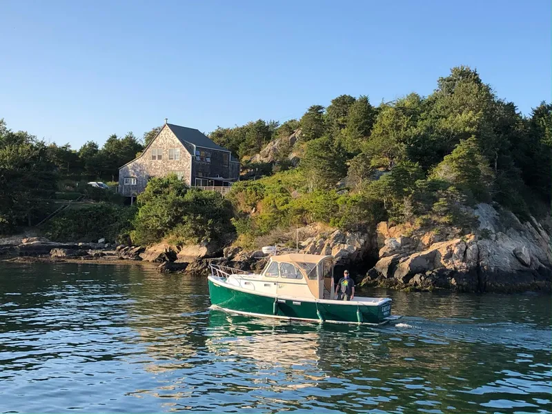 Slide: The Image of 1999 Atlas Boat Works Acadia 25 cruising near rocky shoreline and rustic house. - 0