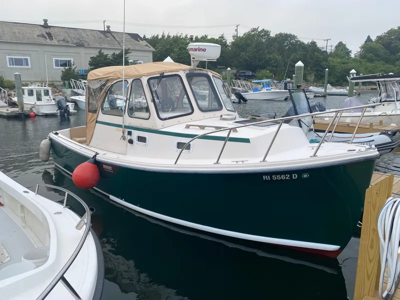 Slide: The Image of 1999 Atlas Boat Works Acadia 25 docked in a marina, featuring a green hull and tan canopy. - 2