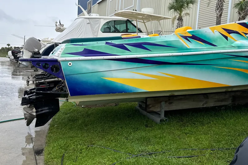 Slide: The Image of Colorful 1997 Hustler 32 speedboat on grass, vibrant graphics, marina background. - 2