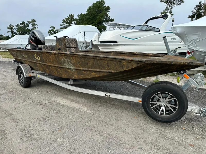 The Image of 2025 G3 Gator Tough 18 CC boat on trailer, camo design, parked outdoors. - 0
