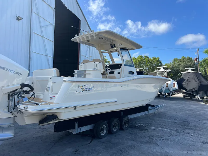 Slide: The Image of 2025 Scout 277 LXF boat on trailer, parked outdoors near a large building. - 5