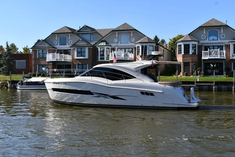 Slide: The Image of 2017 Carver C37 Coupe yacht on a serene waterfront, with elegant homes in the background. - 2