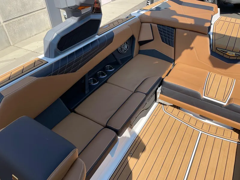 Slide: The Image of 2025 Nautique Super Air Nautique S23 interior with tan and black seating, cup holders, and teak flooring. - 7