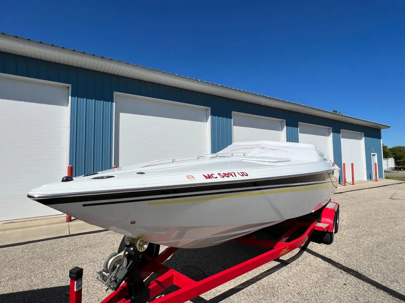 Slide: The Image of 2005 Baja Outlaw boat on red trailer, parked near blue warehouse. - 19