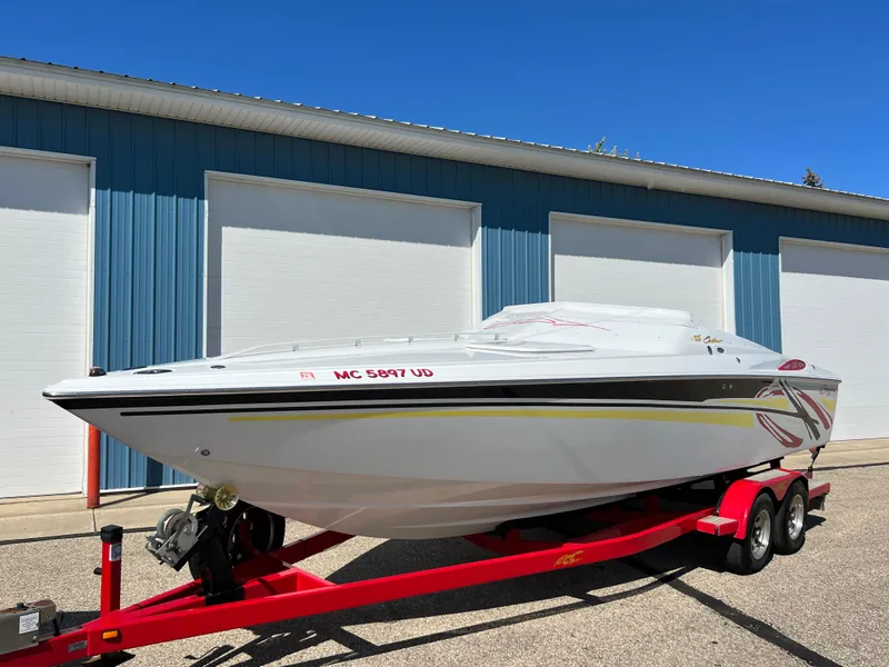 Slide: The Image of 2005 Baja Outlaw boat on red trailer, parked near blue building. - 24