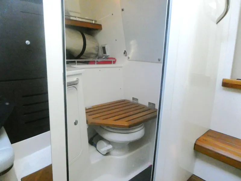 Slide: The Image of 2024 Boston Whaler 350 Realm boat interior with compact bathroom and wooden accents. - 21