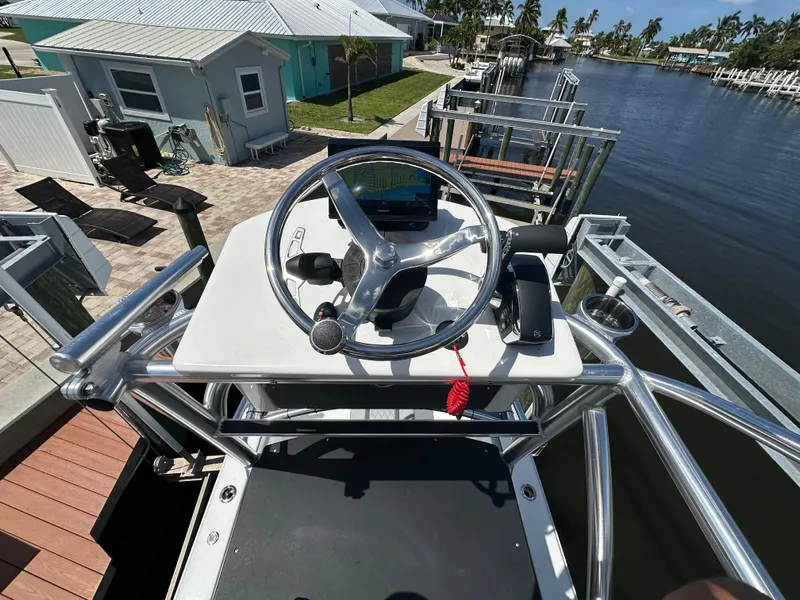 Slide: The Image of 2024 Lake & Bay 25 Open boat helm with steering wheel, docked by waterfront homes. - 16
