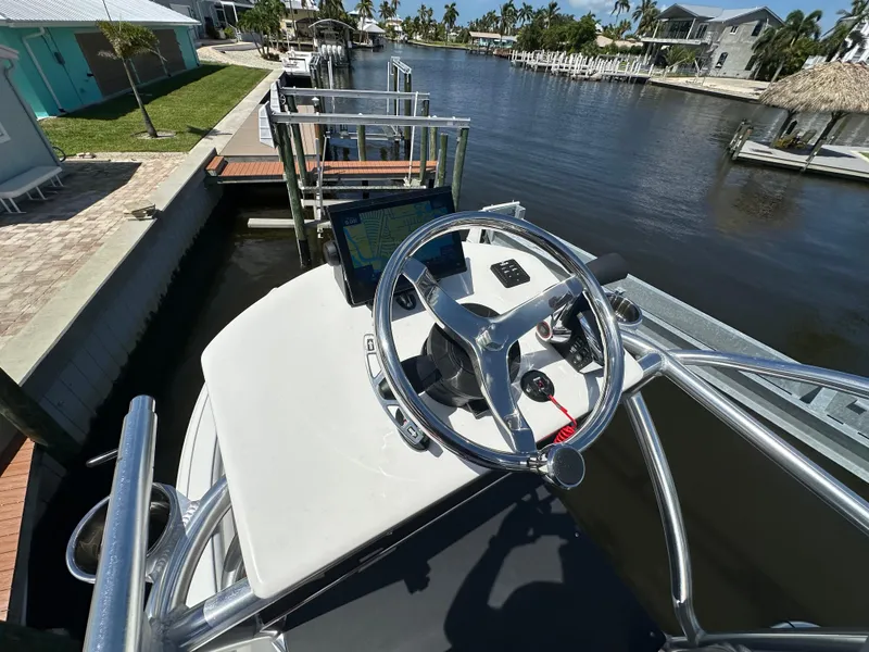 Slide: The Image of 2024 Lake & Bay 25 Open boat steering wheel and console at a dockside canal. - 17