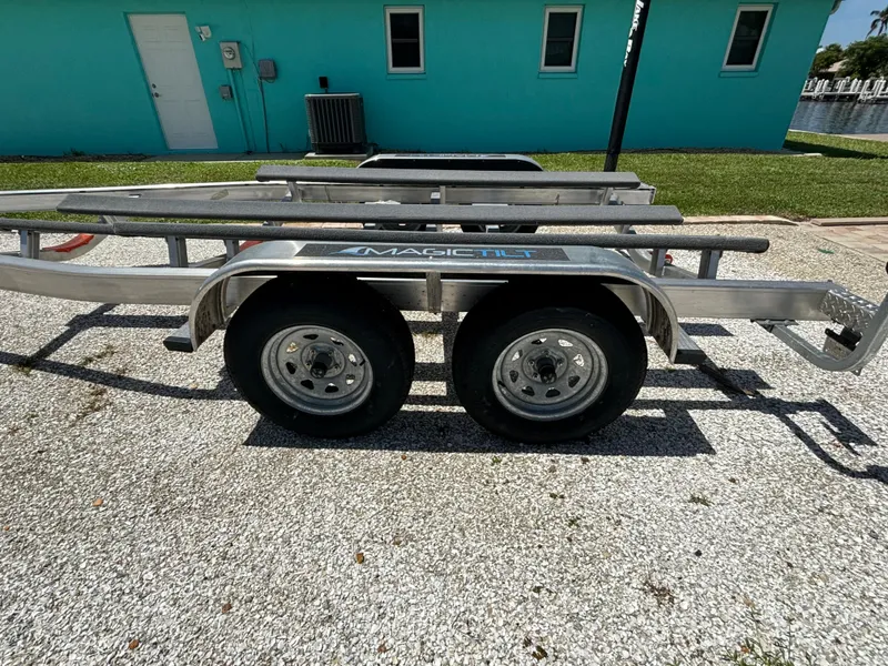 Slide: The Image of 2024 Lake & Bay 25 Open boat trailer parked on gravel near turquoise building. - 24