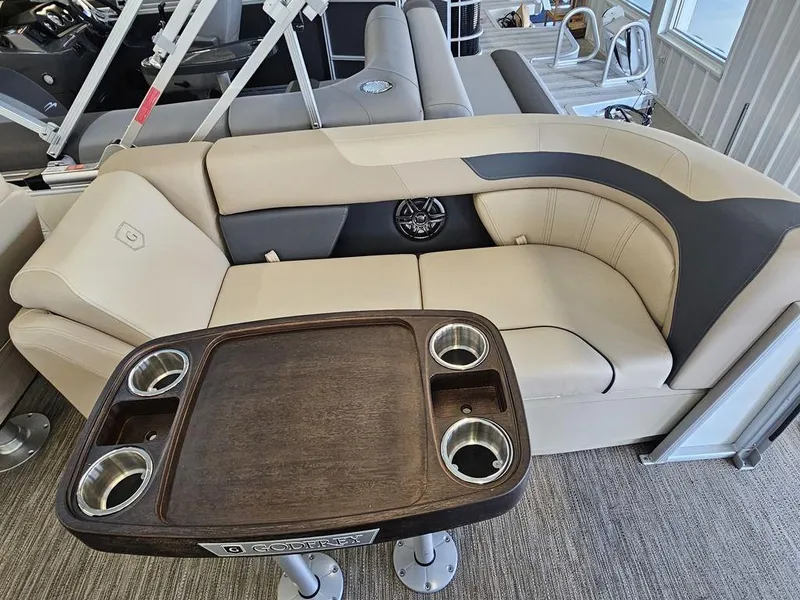 Slide: The Image of 2025 Godfrey SWEETWATER 2286 SB boat interior with beige seating and wooden table. - 6