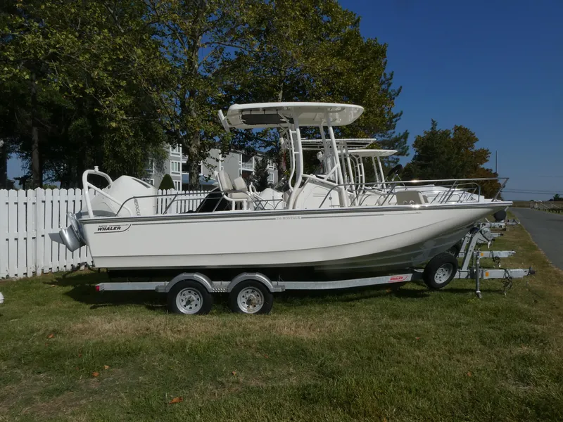 Slide: The Image of 2025 Boston Whaler 210 Montauk boat on trailer, parked on grass. - 2