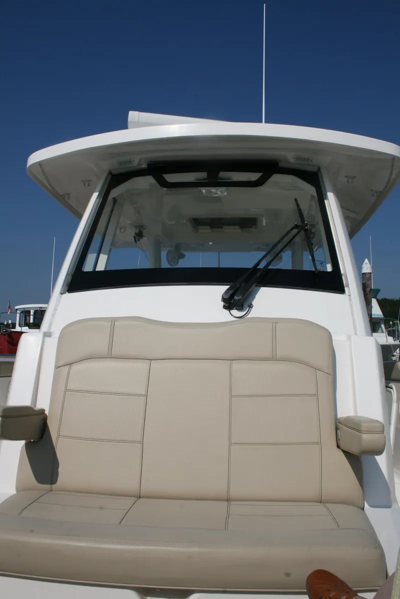 Slide: The Image of 2018 Pursuit S 328 Sport boat with beige seating and windshield, docked under clear blue sky. - 19