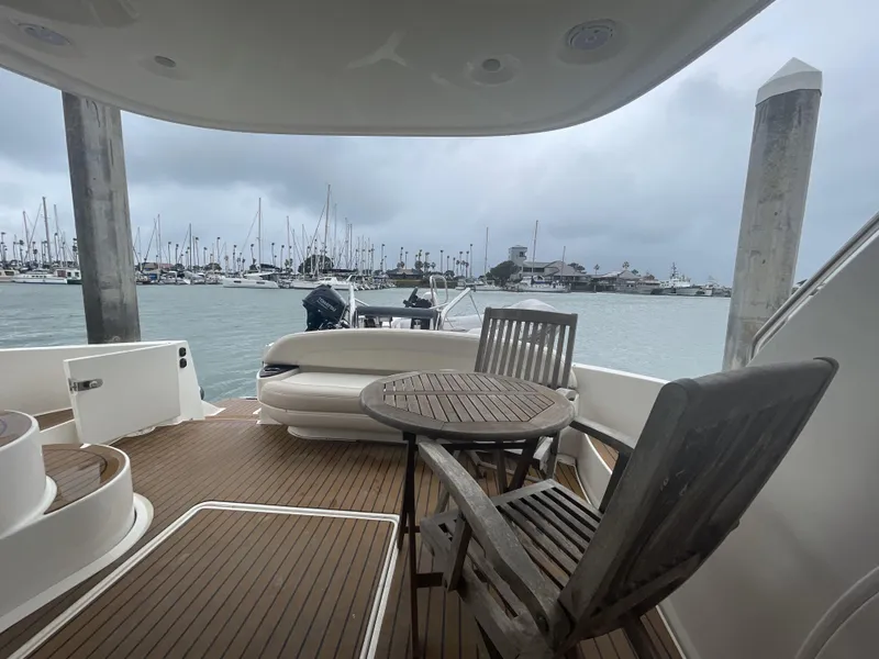 Slide: The Image of 2011 Meridian 441 Sedan Bridge yacht deck with wooden chairs, table, and marina view. - 1