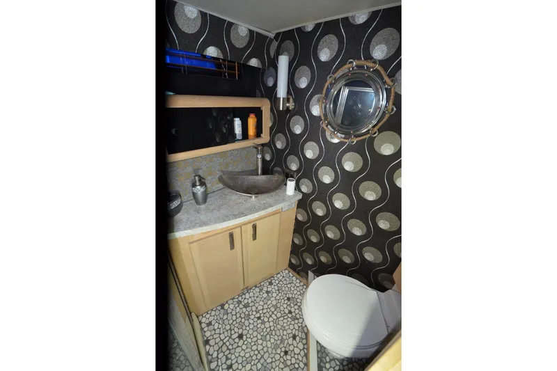 Slide: The Image of 1989 Silverton 46 Aft Cabin bathroom with modern sink, patterned wallpaper, and porthole window. - 47