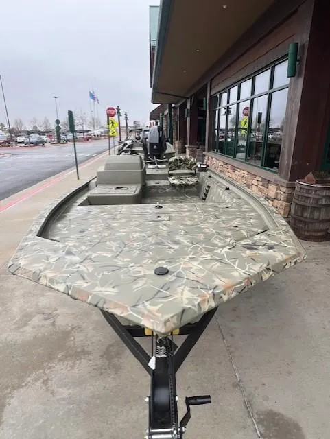 Slide: The Image of 2025 Tracker Grizzly 1754 SC boat with camouflage design parked outside a building. - 2