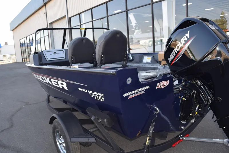 Slide: The Image of 2025 Tracker Pro Guide V-16 WT boat with Mercury engine, parked outside a building. - 2